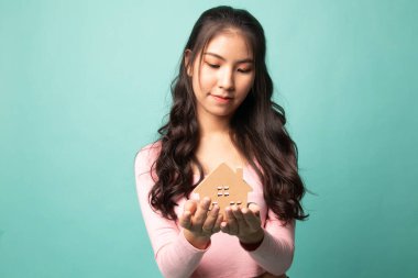 Cyan arka planında ev modeli olan mutlu genç Asyalı kadın.