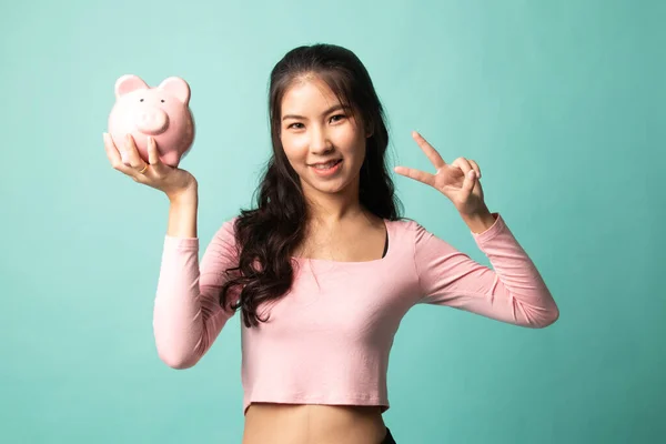 Azji Kobieta Pokazać Znak Zwycięstwa Banku Świnia Monety Tle Cyjan — Zdjęcie stockowe
