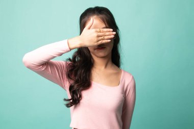 Genç Asyalı kadın, elini cyan arka planda tutarak gözlerini kapatıyor.