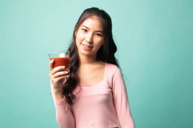 Genç Asyalı kadın arka planda domates suyu içiyor.