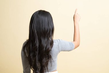 Asyalı bir kadın bej arka planda parmağıyla ekrana dokunuyor.