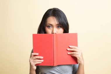 Kitabı olan genç bir Asyalı kadın bej arka planda yüzünü kapatıyor.