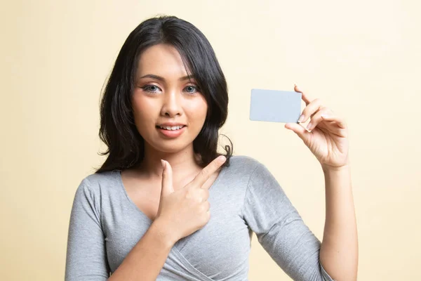 年轻的亚洲女人指着一张米色背景的空白卡片 — 图库照片