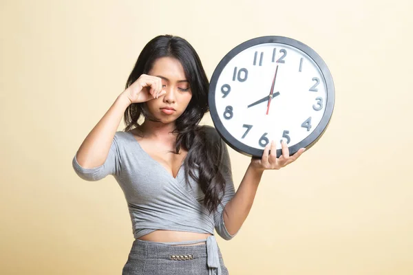 Sleepy young Asian woman with a clock in the morning   on beige background