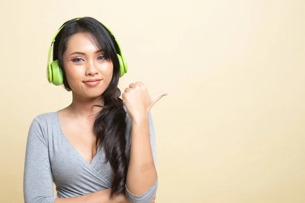 漂亮的亚洲女孩用耳机听音乐 用她的大拇指在米色背景下模仿空间 — 图库照片