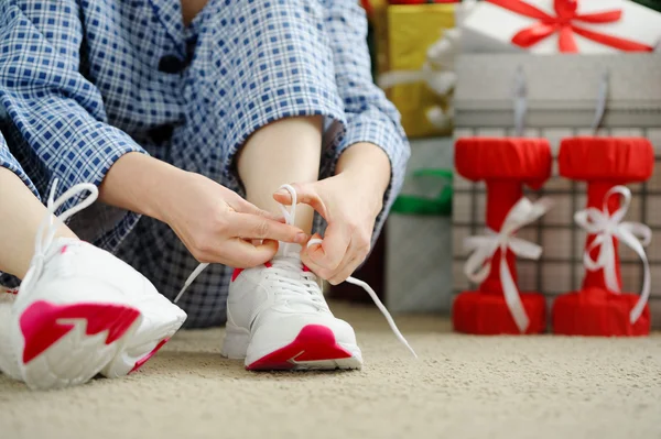 Woman in pajamas ties the laces of athletic shoes.