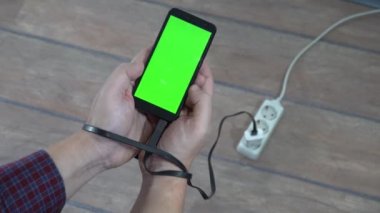 Modern problem kavramı. Elinde boş ekranlı cep telefonu olan bir adam elektrik bağlantısına bağlı. Eller şarj kablosuna bağlı..