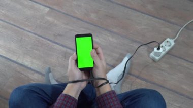 Modern problem kavramı. Elinde boş ekranlı cep telefonu olan bir adam elektrik bağlantısına bağlı. Eller şarj kablosuna bağlı..