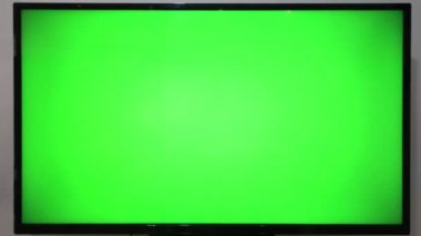 TV kumandasını gösteren ve yeşil ekranlı bir televizyonun önündeki düğmelere basan kişi