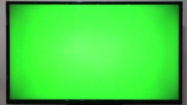 TV kumandasını gösteren ve yeşil ekranlı bir televizyonun önündeki düğmelere basan kişi