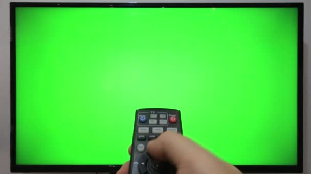 緑の画面のテレビの前でテレビのリモコンを指してボタンを押す者 — ストック動画