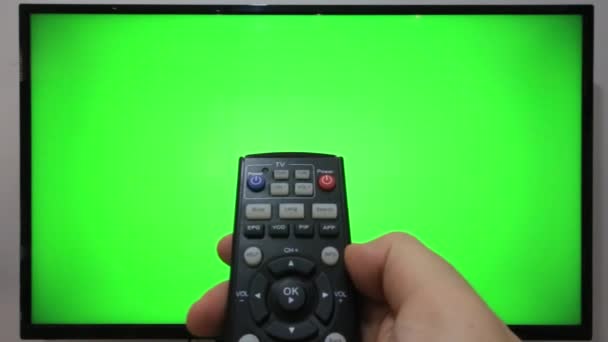 緑の画面のテレビの前でテレビのリモコンを指してボタンを押す者 — ストック動画