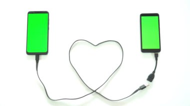 Kalp şeklinde bir USB kabloyla iki akıllı telefonu birbirine bağlamak. Uzak mesafe ilişkisi kavramı.