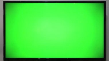 TV kumandasını gösteren ve yeşil ekranlı bir televizyonun önündeki düğmelere basan kişi