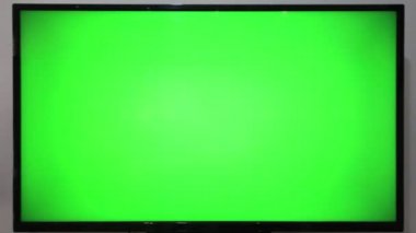 TV kumandasını gösteren ve yeşil ekranlı bir televizyonun önündeki düğmelere basan kişi