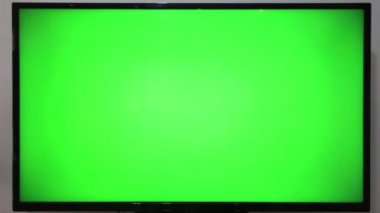 TV kumandasını gösteren ve yeşil ekranlı bir televizyonun önündeki düğmelere basan kişi