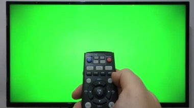 TV kumandasını gösteren ve yeşil ekranlı bir televizyonun önündeki düğmelere basan kişi