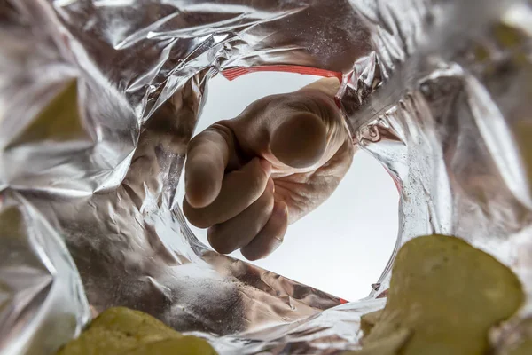 Creative view from inside a bag of potato chips with a hand reaching for a chip