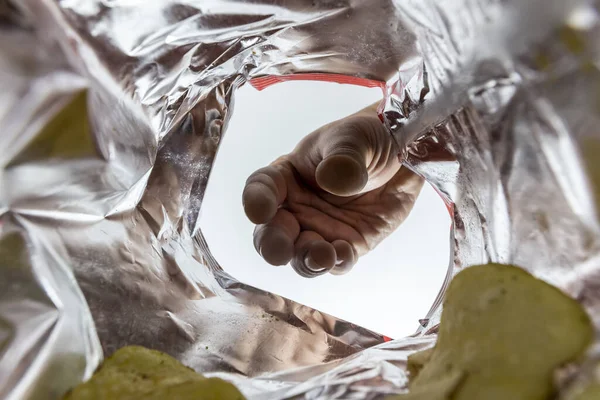 Creative view from inside a bag of potato chips with a hand reaching for a chip