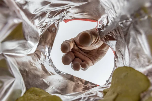 Creative view from inside a bag of potato chips with a hand reaching for a chip