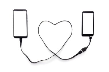 Kalp şeklinde bir USB kabloyla iki akıllı telefonu birbirine bağlamak. Uzak mesafe ilişkisi kavramı.