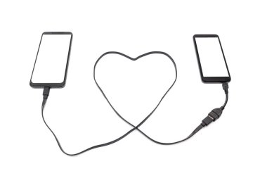 Kalp şeklinde bir USB kabloyla iki akıllı telefonu birbirine bağlamak. Uzak mesafe ilişkisi kavramı.