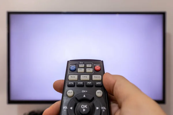 Bir TV kumandasını işaret eden ve boş ekranlı bir televizyonun önündeki düğmelere basan kişi