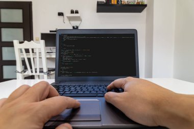 Uzaktan kumanda merkezi. Evdeki bir dizüstü bilgisayarda kod yazan bir programcının düşük açılı görüntüsü.