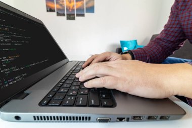 Uzaktan kumanda merkezi. Evdeki bir dizüstü bilgisayarda kod yazan bir programcının düşük açılı görüntüsü.
