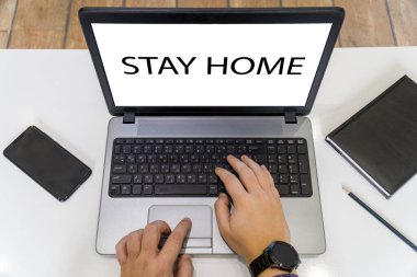 Ekranda evde kalma mesajı olan ve dizüstü bilgisayarda çalışan bir kişinin genel görünümü