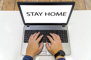 Ekranda evde kalma mesajı olan ve dizüstü bilgisayarda çalışan bir kişinin genel görünümü