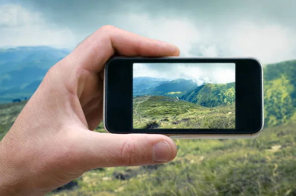Teléfono en una mano del hombre, fotografías de paisajes de montaña en su teléfono inteligente, vista lateral, selfie — Foto de Stock