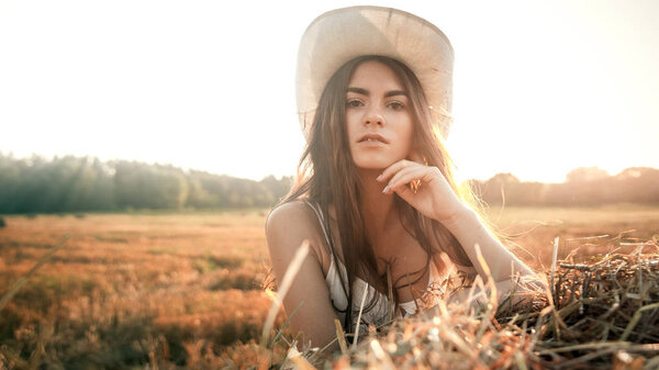 Rural girl on straw bale in a field, a cowboy hat, Beautiful woman on a haystack
