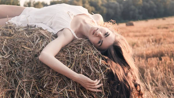 Ragazza rurale su balla di paglia in un campo, Bella donna su un pagliaio Foto Stock Royalty Free