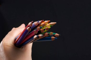 İş kavramları: siyah arka planda elde renkli kalemler