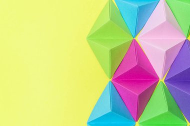 Sarı arka plan üzerinde renkli origami piramitleri ile kopya alanı sol tarafında.
