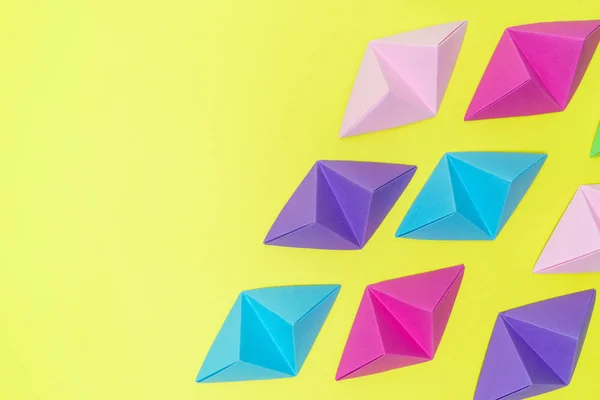Composición abstracta de tetraedros de origami de colores variables sobre fondo amarillo con espacio de copia en el lado izquierdo . — Foto de Stock