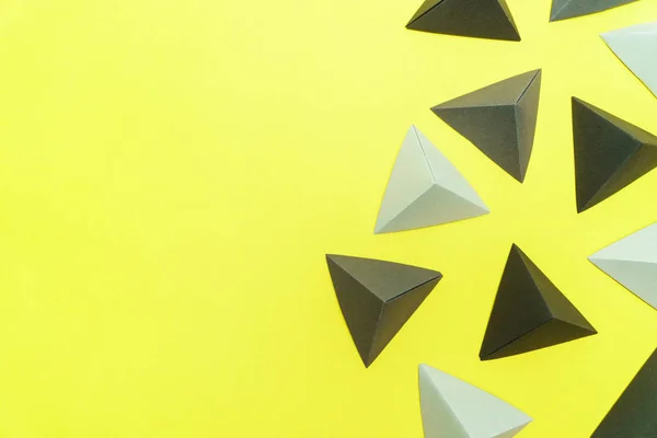 Tetraedros en origami gris y negro sobre fondo amarillo con espacio de copia en el lado izquierdo . — Foto de Stock