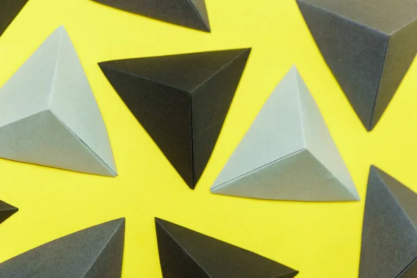 Tetraedros en origami gris y negro sobre fondo amarillo vista superior . — Foto de Stock