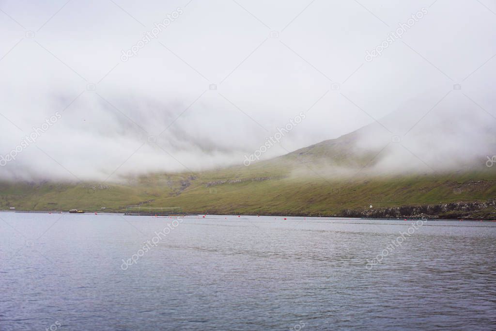 Foggy coastline of Vagar village, Faroe Islands. Thick fog covering green hills.