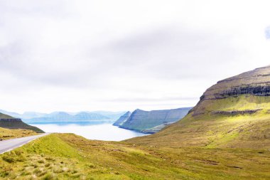 Yeşil kayalıklı fiyort ve arabasız bir yol. Eysturoy Adası, Faroe, Danimarka.
