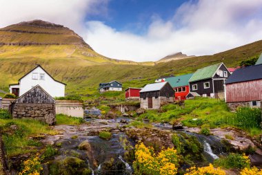 Funningur köyünün renkli evleri küçük bir nehir ve arka planda göze çarpan dağlar. Faroe Adaları, Danimarka.