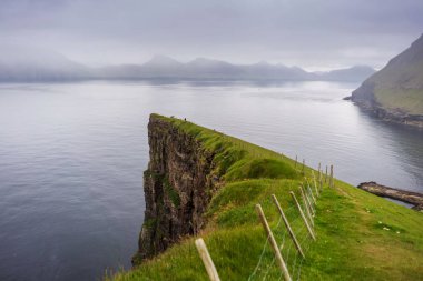 Uçurumun kenarında yürüyüş yolu ve ufukta görünen uzak adalar. Faroe Adaları, Gjogv Köyü.