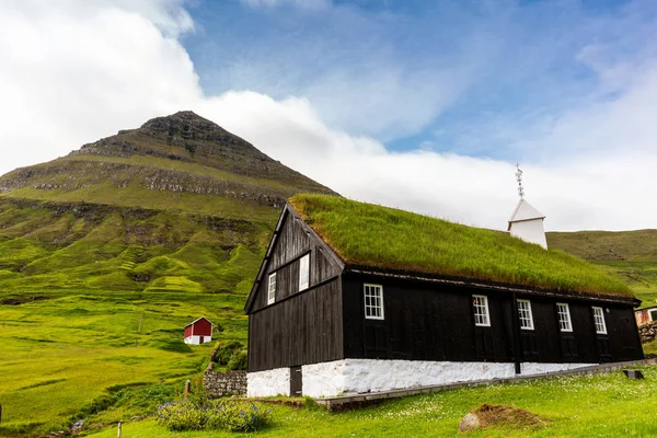 Eski Faroe ahşap kilisesi, çimen çatısı ve arka planda bulutlarla kaplı dağ. Faroe Adaları, Danimarka.