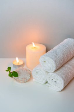 Gri arkaplanda beyaz havlu, mum ve bir fincan deniz tuzu içeren dikey konsept fotoğraftaki spa prosedürü.