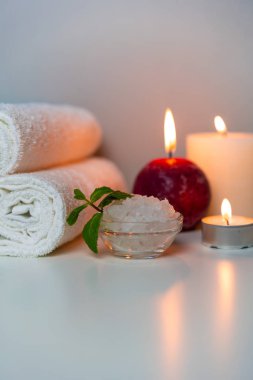 Aromaterapi ve güzellik salonundaki fotoğraflarda gri arka planda bir yığın havlu, mum ışığı ve bir fincan deniz tuzu var..
