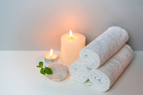 SPA procedure concept photo on grey background with stack of white towels, candles and cup of sea salt.