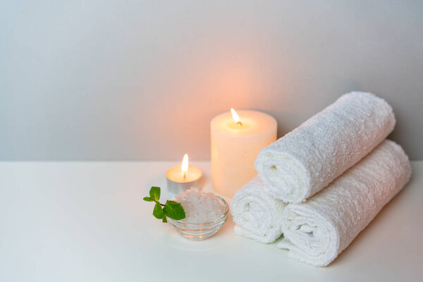 SPA treatments concept photo on grey background with stack of white towels, candles and cup of sea salt.