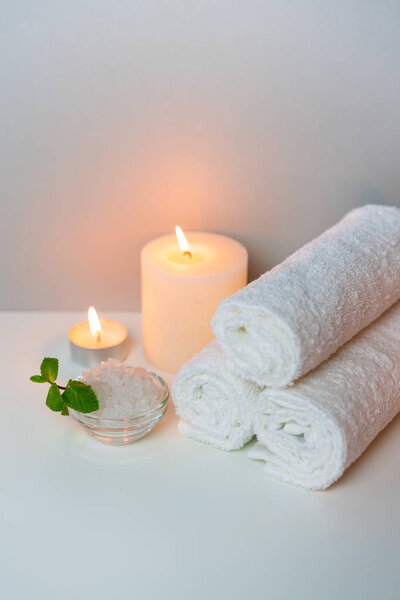 SPA procedure at salon vertical concept photo on grey background with stack of white towels, candles and cup of sea salt.