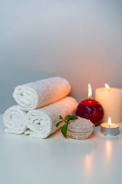 Natural health treatments of SPA, vertical orientation photo. White towels, sea salt in a cup, candles.